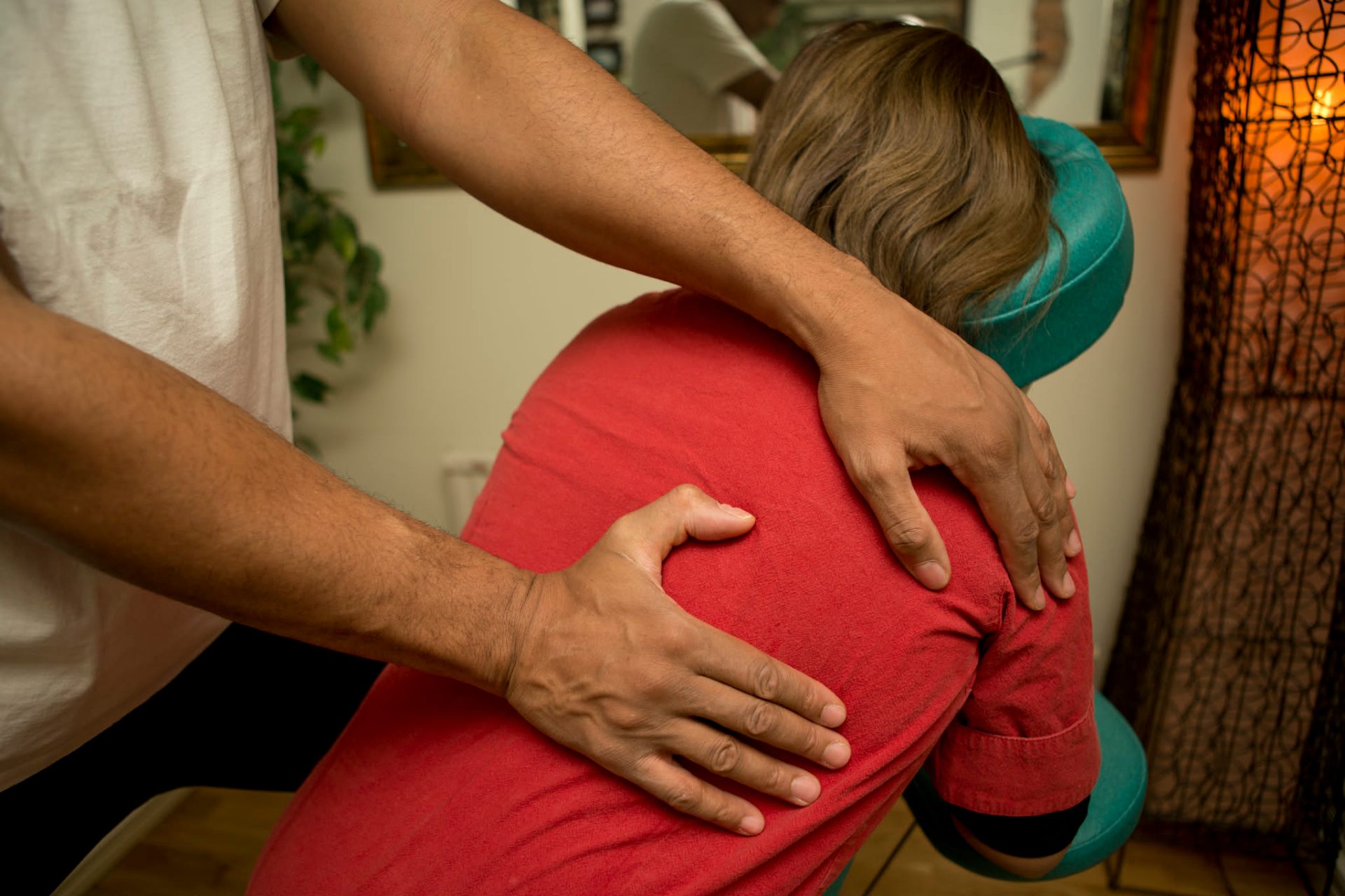 Behandling i energimassagestol — händer arbetar med nacke och rygg i lugn, varm miljö.